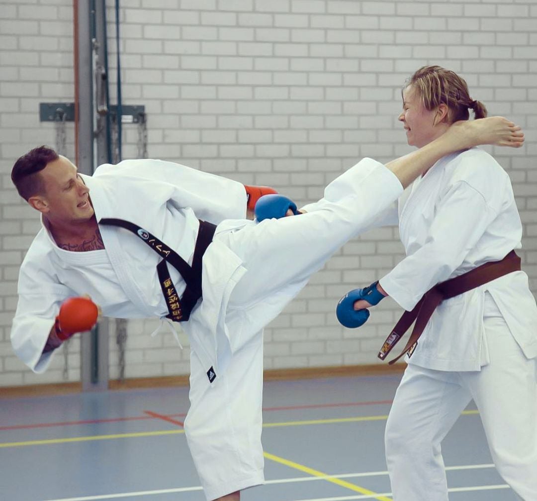 Twee volwassen karateka's oefenen samen: een hoge trap wordt afgeweerd